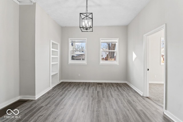 unfurnished dining area featuring baseboards, an inviting chandelier, and wood finished floors