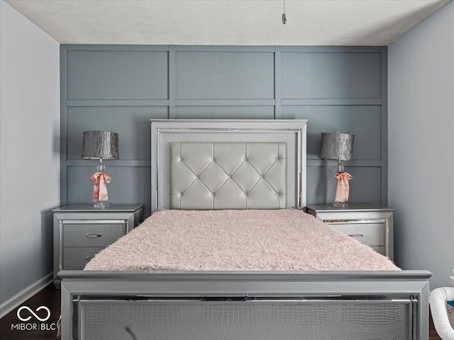 bedroom with a decorative wall, dark wood-style floors, baseboards, and a textured ceiling