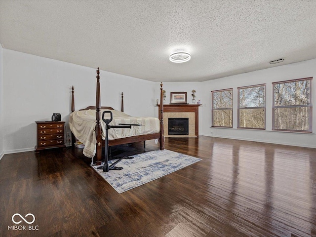 bedroom featuring visible vents, a tile fireplace, a textured ceiling, and wood finished floors