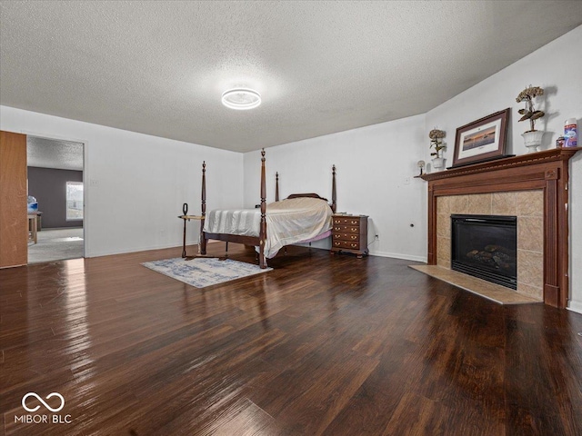 bedroom with a tiled fireplace, a textured ceiling, baseboards, and wood finished floors