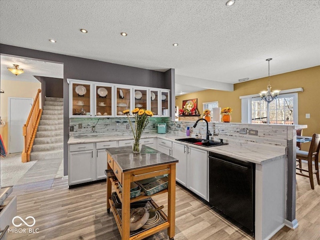 kitchen featuring a peninsula, a sink, decorative backsplash, black dishwasher, and glass insert cabinets