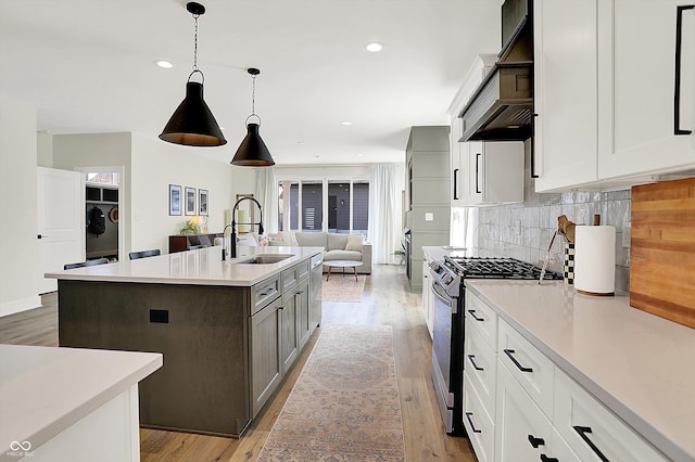 kitchen with backsplash, stainless steel range with gas cooktop, light countertops, light wood-style flooring, and a sink