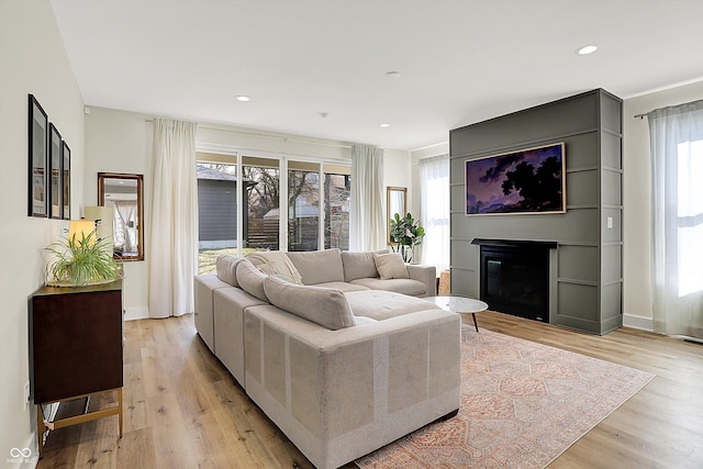 living area with a glass covered fireplace, recessed lighting, baseboards, and light wood-style floors