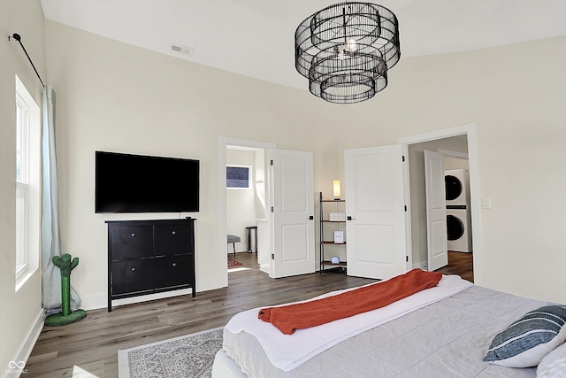 bedroom featuring visible vents, baseboards, stacked washing maching and dryer, wood finished floors, and a notable chandelier