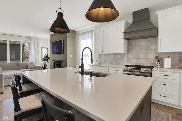 kitchen featuring stainless steel gas range oven, a kitchen island with sink, a sink, open floor plan, and custom exhaust hood