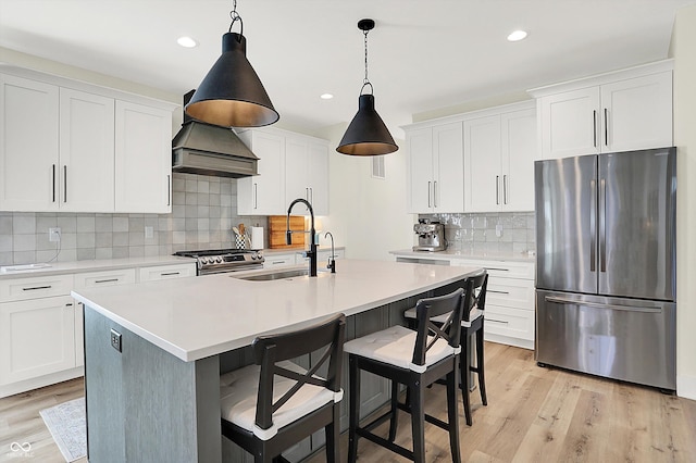 kitchen featuring light wood finished floors, a center island with sink, a sink, appliances with stainless steel finishes, and light countertops