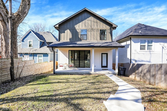 rear view of house featuring a porch, a fenced backyard, board and batten siding, and a lawn