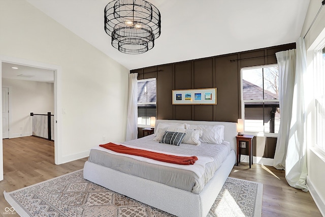 bedroom featuring an inviting chandelier, light wood finished floors, baseboards, and lofted ceiling