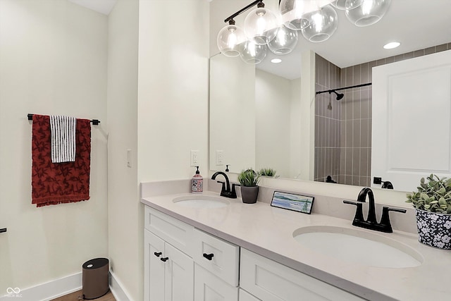 bathroom featuring double vanity, tiled shower, baseboards, and a sink