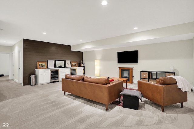 living room with beverage cooler, a glass covered fireplace, recessed lighting, baseboards, and light colored carpet