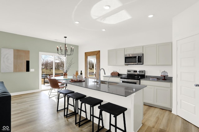 kitchen with a chandelier, a breakfast bar, light wood-style floors, stainless steel appliances, and a sink