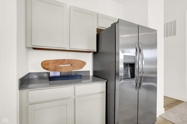 kitchen featuring baseboards, visible vents, light wood-type flooring, white cabinets, and stainless steel fridge