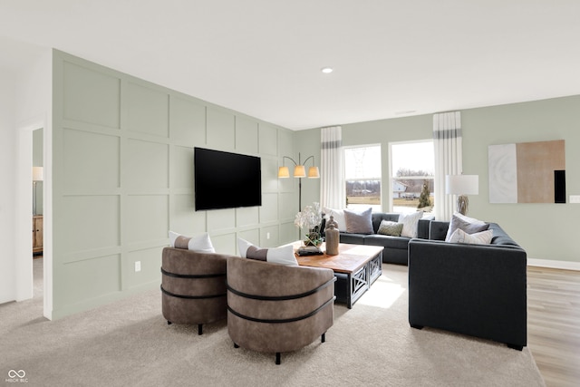 living area featuring recessed lighting, a decorative wall, and light colored carpet