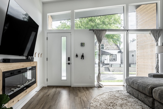 foyer featuring a glass covered fireplace, a towering ceiling, baseboards, and wood finished floors