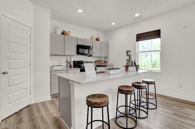 kitchen with visible vents, black microwave, a kitchen bar, electric range oven, and gray cabinets