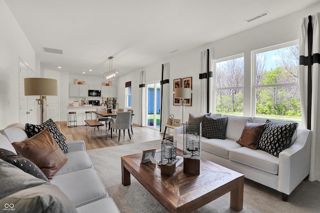 living area with visible vents, a notable chandelier, a healthy amount of sunlight, and light wood finished floors