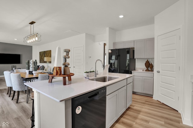 kitchen featuring light wood-type flooring, black appliances, a sink, open floor plan, and light countertops