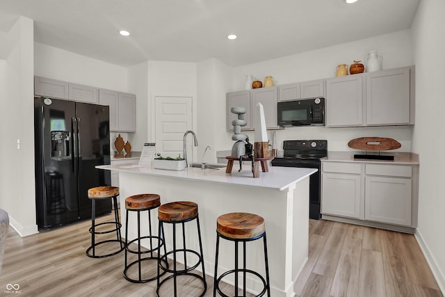 kitchen featuring black appliances, light wood-style flooring, a sink, a kitchen breakfast bar, and light countertops