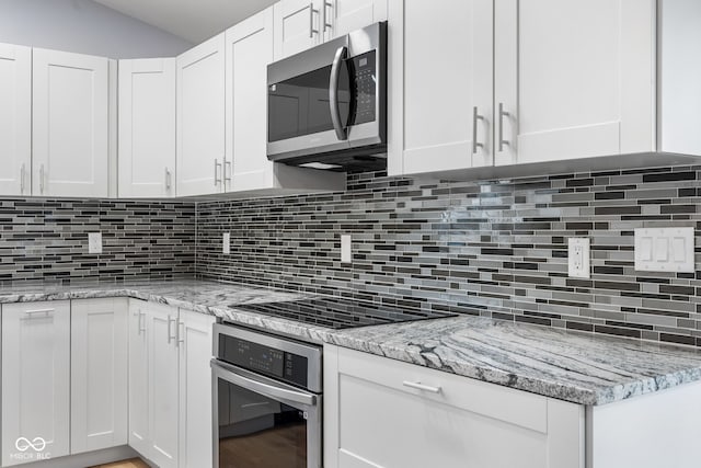 kitchen with white cabinets, light stone countertops, backsplash, and stainless steel appliances