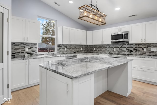 kitchen featuring stainless steel microwave, light wood-style flooring, visible vents, and lofted ceiling