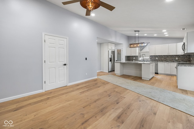 kitchen featuring lofted ceiling, decorative backsplash, light wood-style floors, stainless steel refrigerator with ice dispenser, and white cabinetry