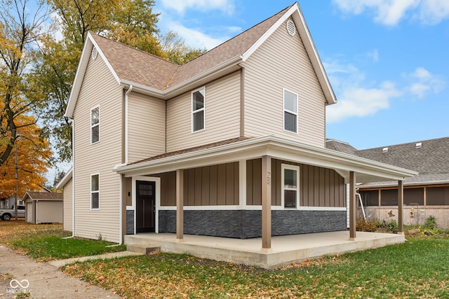 view of front of home with stone siding, board and batten siding, a front yard, and roof with shingles