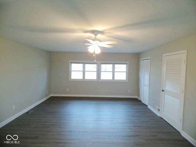 unfurnished bedroom featuring dark wood-type flooring, visible vents, baseboards, and two closets