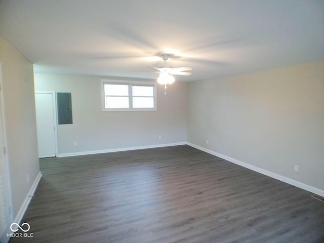 spare room with electric panel, a ceiling fan, dark wood-type flooring, and baseboards