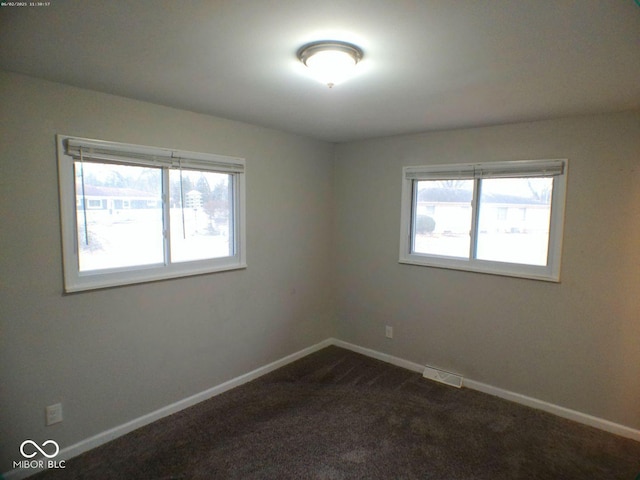 empty room with baseboards, visible vents, and dark colored carpet