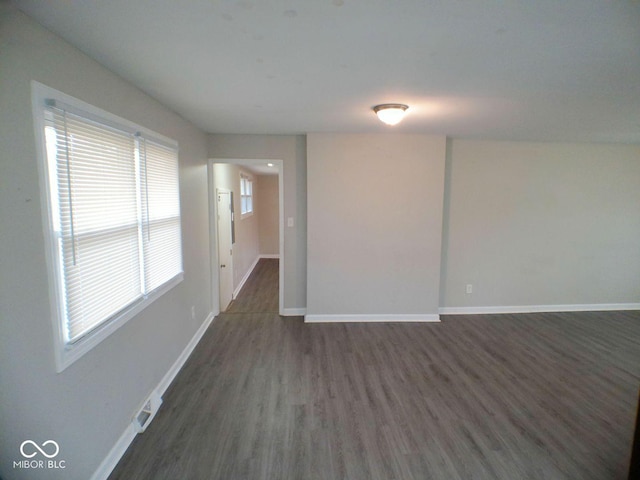 unfurnished room with visible vents, dark wood-style floors, and baseboards