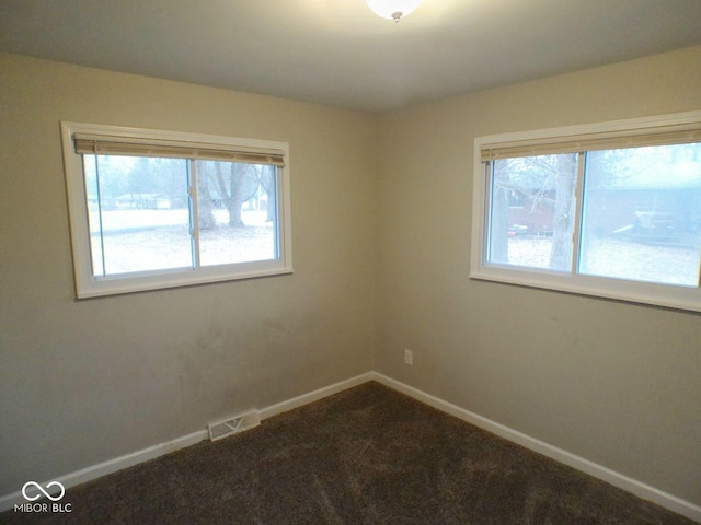 spare room with visible vents, baseboards, and dark colored carpet