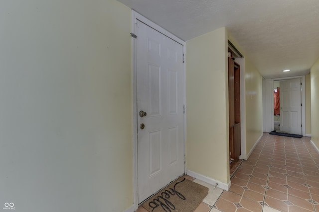 hallway with light tile patterned floors, a textured ceiling, and baseboards