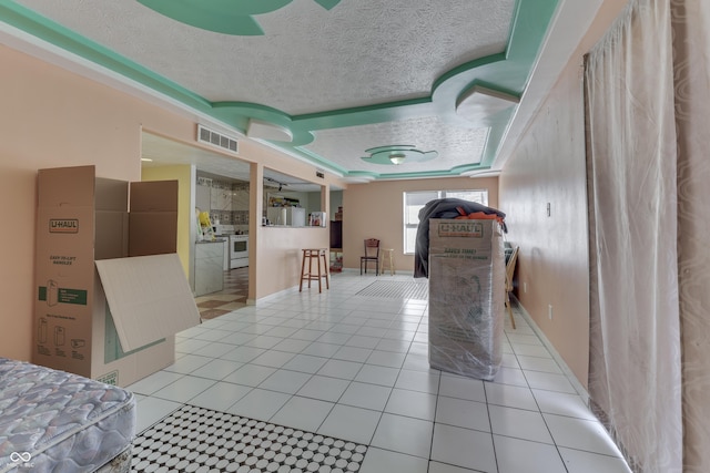 interior space with visible vents, light tile patterned flooring, electric range, a textured ceiling, and a raised ceiling