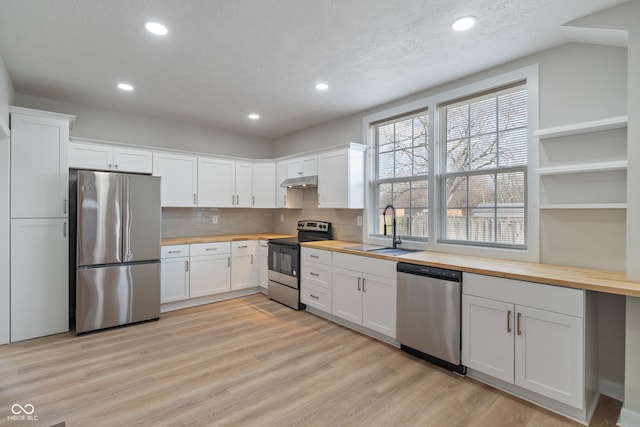 kitchen featuring light wood-style flooring, a sink, under cabinet range hood, appliances with stainless steel finishes, and wooden counters