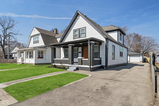 view of front facade featuring a front yard, an outbuilding, covered porch, and a shingled roof