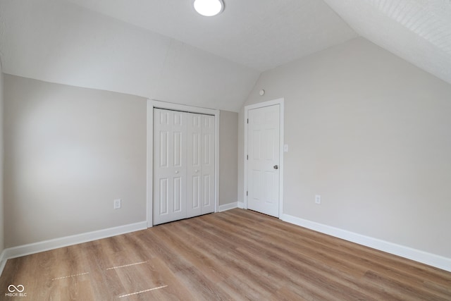 unfurnished bedroom featuring lofted ceiling, light wood-style floors, baseboards, and a closet