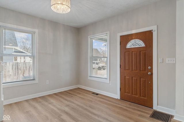 foyer entrance featuring a notable chandelier, baseboards, visible vents, and light wood finished floors