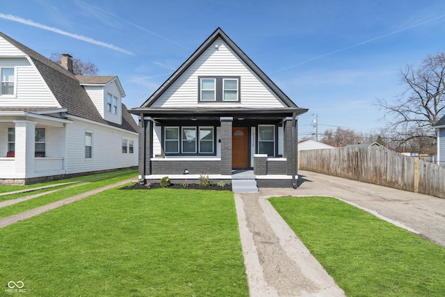 view of front of property with fence, a porch, concrete driveway, a front lawn, and brick siding