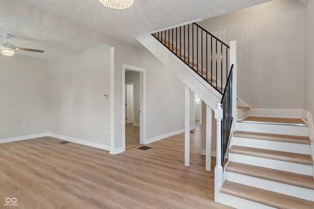 staircase featuring ceiling fan, visible vents, a textured ceiling, and wood finished floors