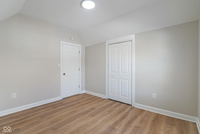 unfurnished bedroom featuring baseboards, light wood-type flooring, and lofted ceiling