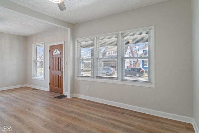 foyer entrance with a ceiling fan, visible vents, baseboards, light wood finished floors, and a textured ceiling