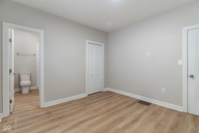 unfurnished bedroom with ensuite bath, baseboards, visible vents, and light wood finished floors