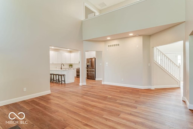 unfurnished living room featuring visible vents, baseboards, light wood-type flooring, a high ceiling, and a sink