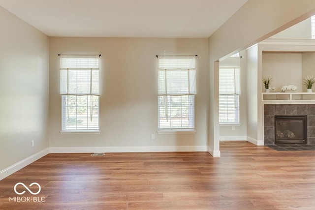 unfurnished living room with a tiled fireplace, baseboards, and wood finished floors