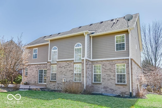 back of property with a yard, brick siding, and roof with shingles