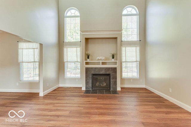 unfurnished living room with baseboards, light wood-style floors, a towering ceiling, and a tiled fireplace