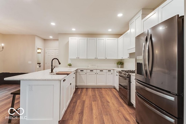 kitchen with a sink, stainless steel fridge, a peninsula, white cabinets, and range with two ovens