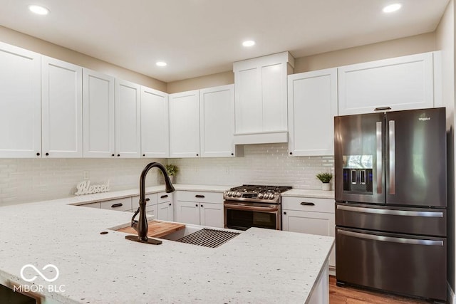 kitchen with a sink, light stone counters, appliances with stainless steel finishes, and white cabinets