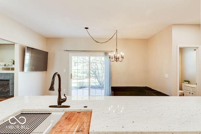 kitchen with a sink, an inviting chandelier, a fireplace, light stone countertops, and hanging light fixtures