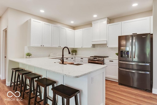 kitchen featuring a kitchen breakfast bar, appliances with stainless steel finishes, a peninsula, light wood-style floors, and a sink